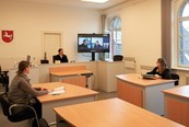 Prozessbeteiligte im Sitzungssaal mit Livebild vom großen Monitor